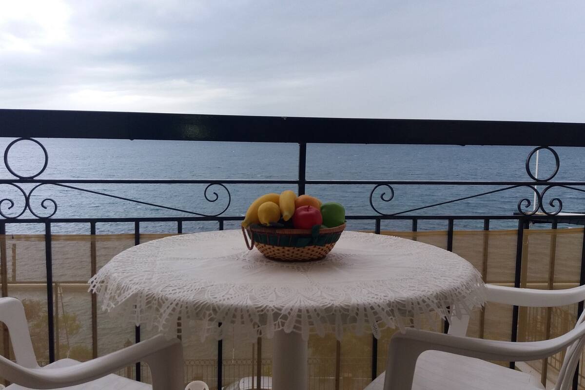 A table with a fruit basket on a balcony with a view of the sea.