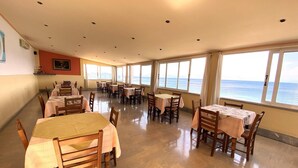 A dining area with tables and chairs, large windows with a view of the sea, and a ceiling with recessed lighting. - El Greco Hotel (Corfu)
