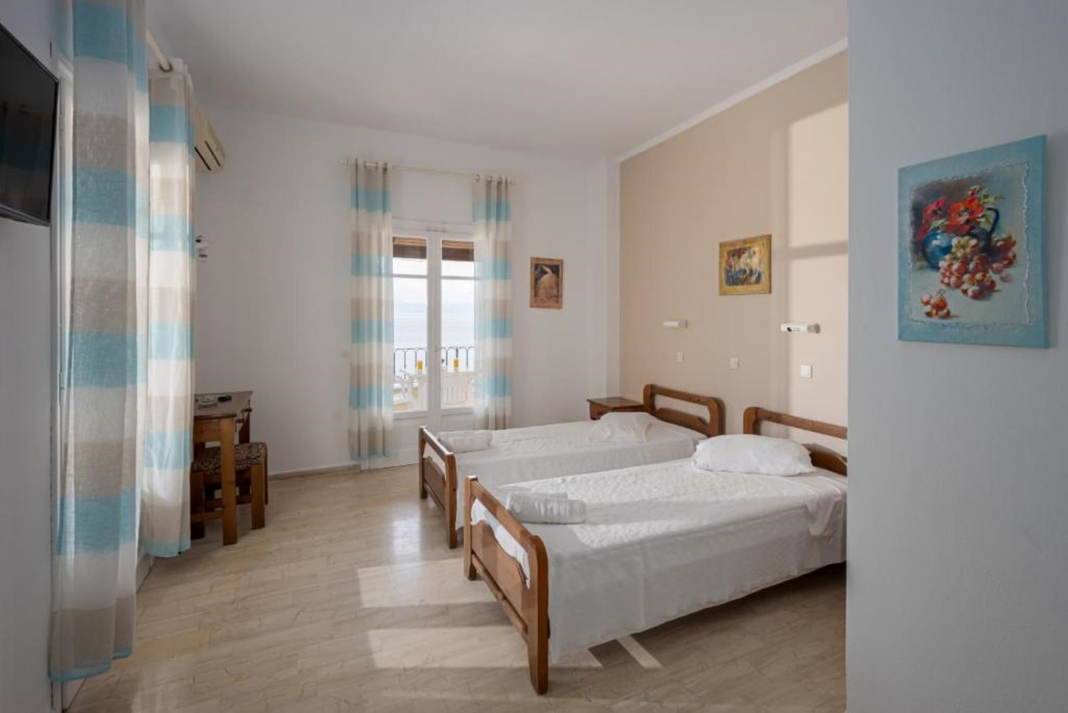 A room with two single beds, a wooden desk, a chair, and a window with curtains.