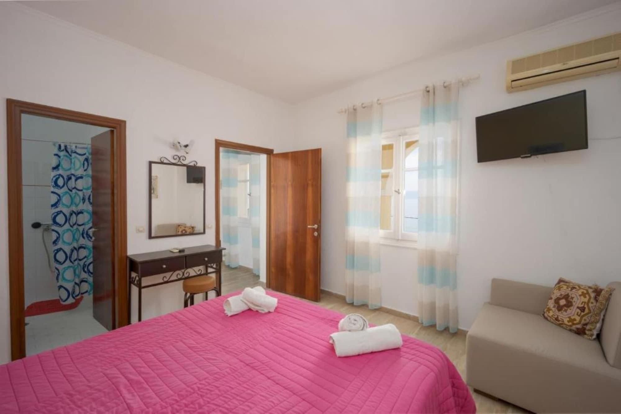 Un dormitorio con cama, cómoda, espejo, puerta, ventana con cortinas, televisor y sofá.