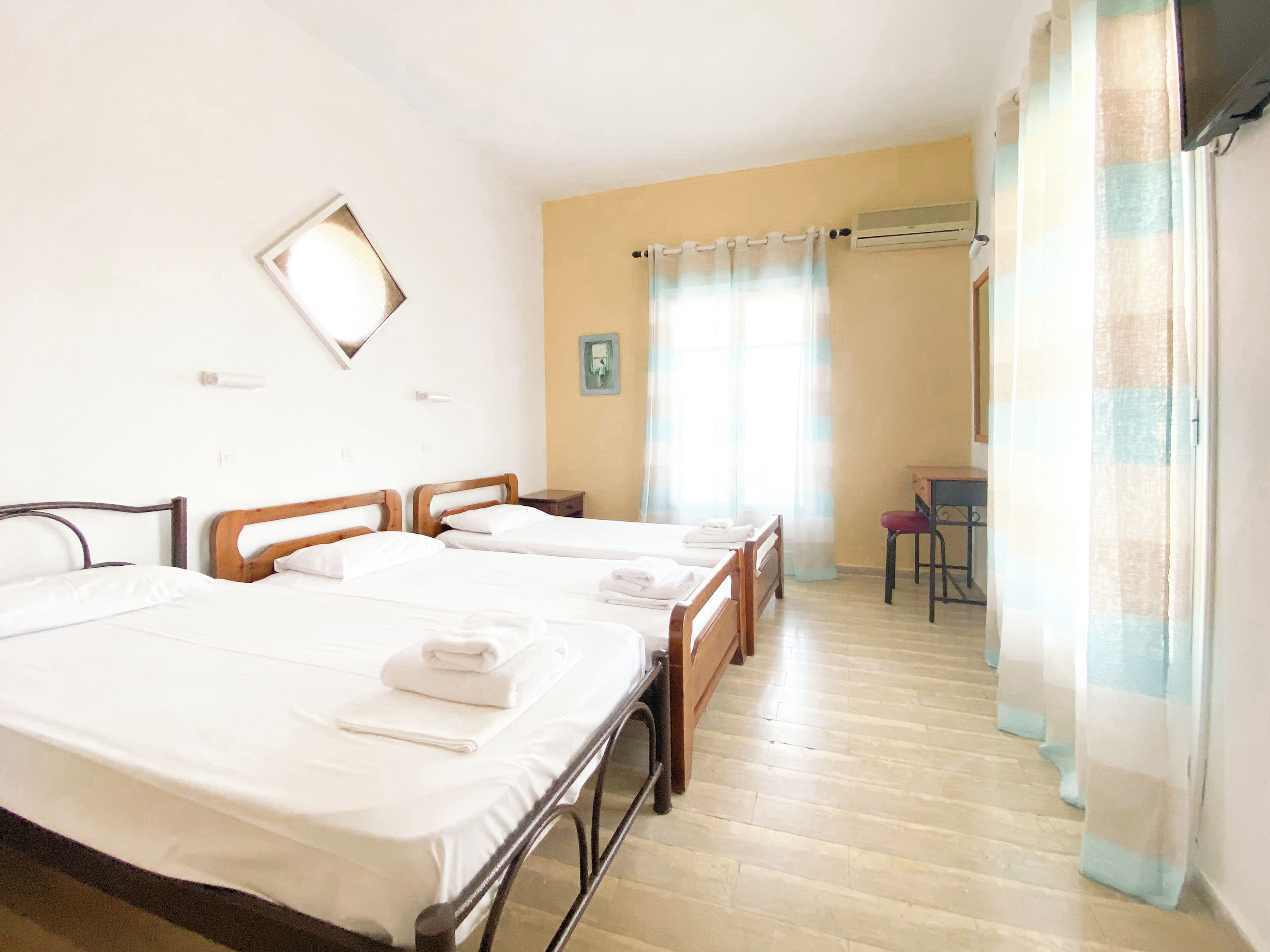 A hotel room with three beds, a desk, a chair, and a window with curtains.