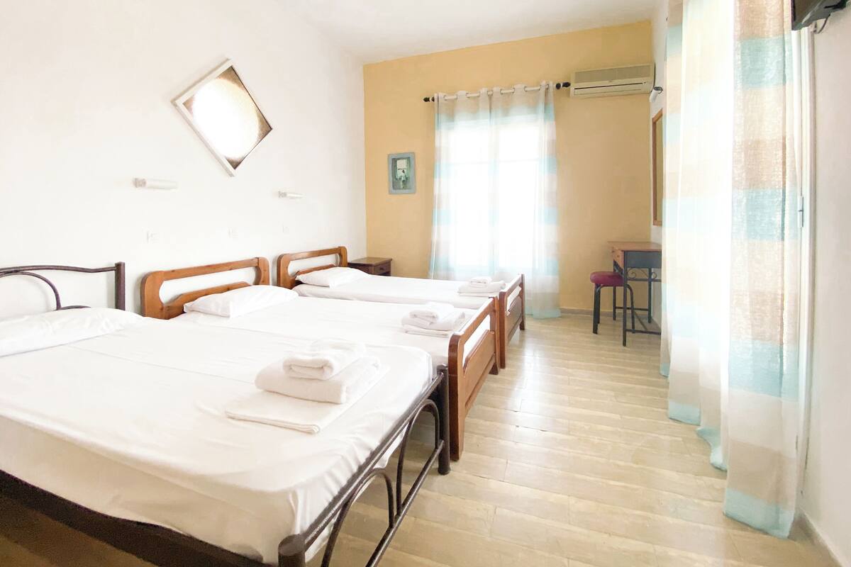 A hotel room with three beds, a desk, a chair, and a window with curtains.