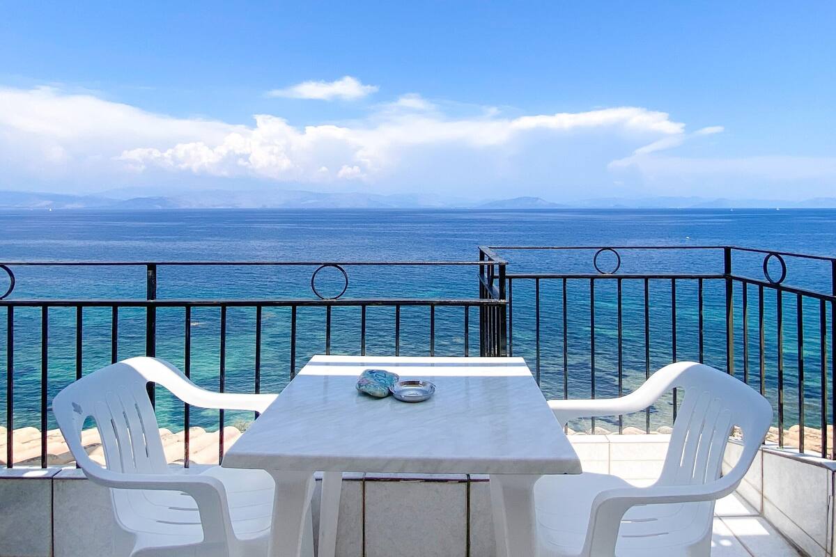 A balcony with a table and chairs overlooking the sea.