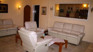 A living room with a sofa, armchairs, a coffee table, and a mirror reflecting the room. - El Greco Hotel (Corfu)