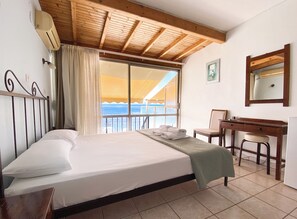 A hotel room with a bed, a desk, a chair, a window with a view of the sea, and a ceiling with wooden beams. - El Greco Hotel (Corfu)