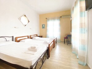 A hotel room with three beds, a desk, a chair, and a window with curtains. - El Greco Hotel (Corfu)