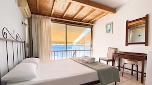 A hotel room with a bed, a desk, a chair, a window with a view of the sea, and a ceiling with wooden beams. - El Greco Hotel (Corfu)