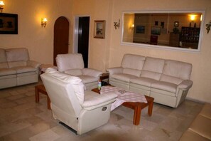 A living room with a sofa, armchairs, a coffee table, and a mirror reflecting the room. - El Greco Hotel (Corfu)