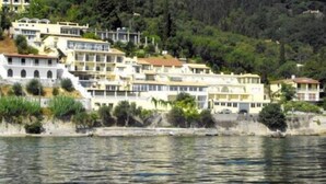 A coastal residential area with multi-story buildings, a waterfront, and a hilly backdrop. - El Greco Hotel (Corfu)