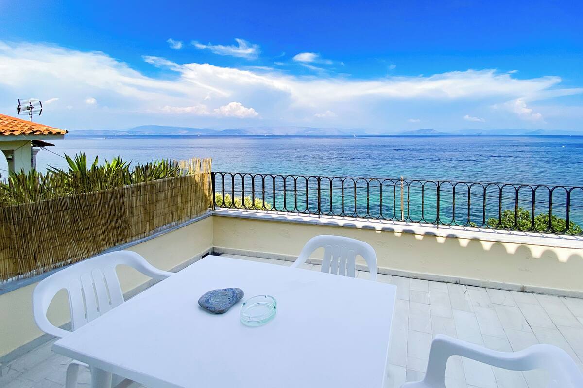A balcony with a table and chairs, a view of the sea, and a bamboo fence.