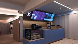 Una recepción con mostrador, una pantalla digital, una cafetera y un refrigerador para bebidas.