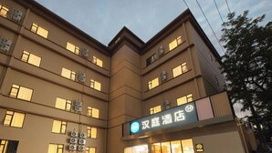 Un hotel de varios pisos con una entrada destacada, unidades de aire acondicionado y un letrero que indica que es un hotel.