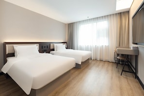 Habitación de hotel con dos camas, un escritorio y un ventanal con cortinas.