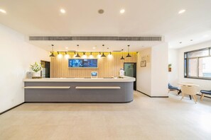 A reception desk with a digital screen, pendant lights, and a small plant. - Hanting Hotel (shanghai North Bund Xinhua Hospital (Shanghai)