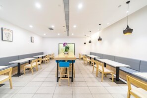 A restaurant with long wooden tables and benches, a central table with a plant, and pendant lighting. - Hanting Hotel (shanghai North Bund Xinhua Hospital (Shanghai)