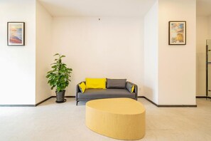 A living room with a grey sofa, yellow cushions, a potted plant, and a round wooden coffee table. - Hanting Hotel (shanghai North Bund Xinhua Hospital (Shanghai)