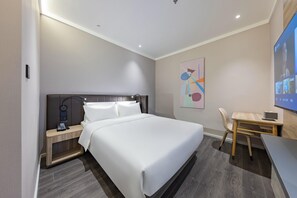 Moderni hotellihuone, jossa on suuri sänky, yöpöytä ja työpöytä tuolilla.