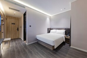 Une chambre d’hôtel moderne avec un grand lit, une table de chevet avec un téléphone et une porte en bois.