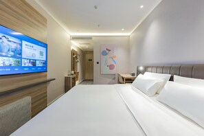 Moderni hotellihuone, jossa on suuri sänky, työpöytä, televisio ja kylpyhuone, joka näkyy avoimesta ovesta.