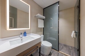 Moderni kylpyhuone, jossa on suuri peili, valkoinen pesuallas, wc ja lasinen suihkukaappi.