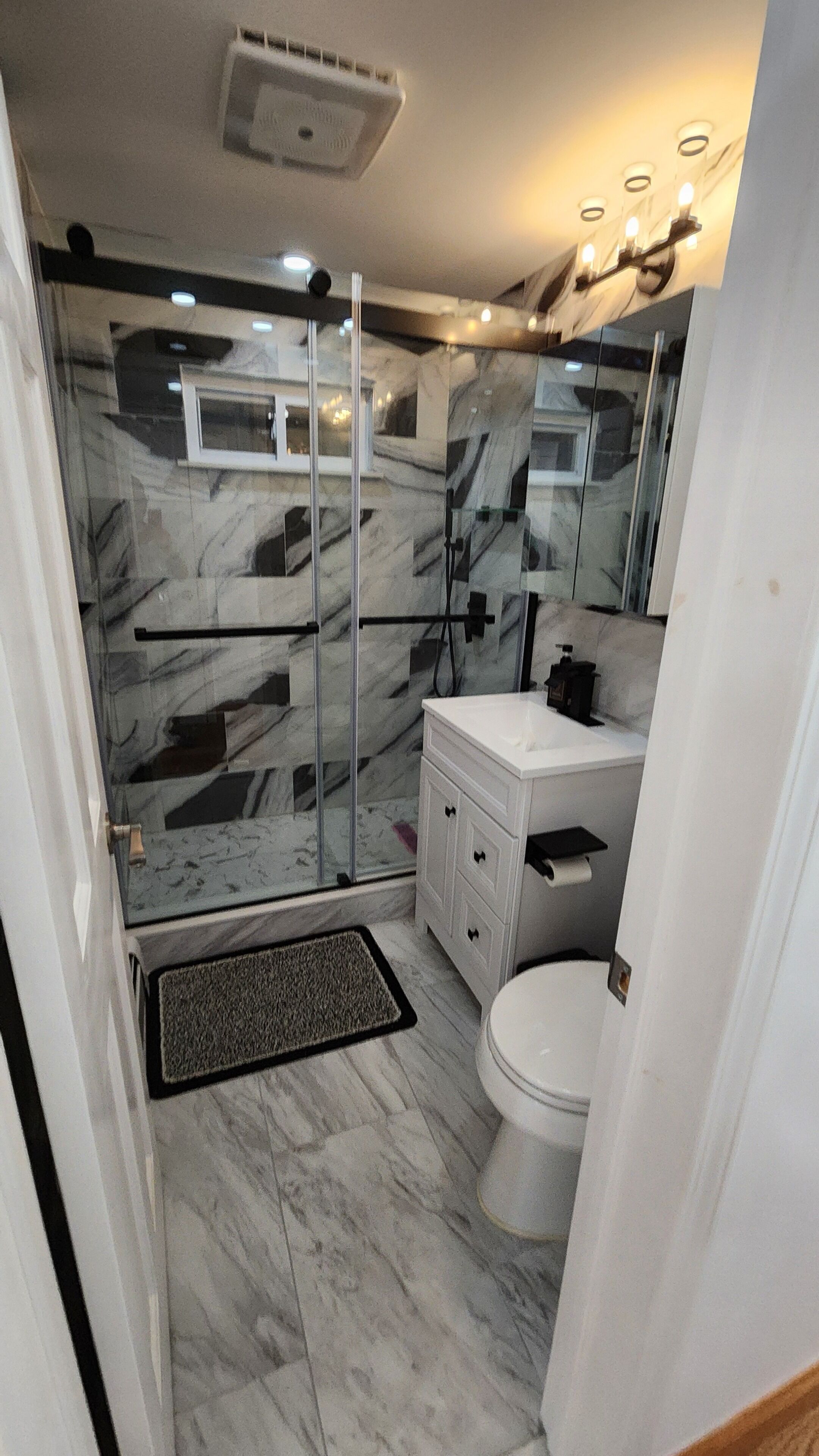 A bathroom with a glass-enclosed shower, a white sink, and a toilet.