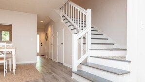 Un escalier avec des rampes blanches et des marches en bois, menant à un couloir doté d’une porte et d’une fenêtre.