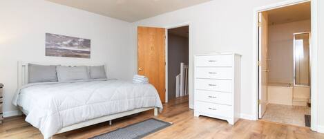 A bedroom with a bed, a nightstand, a dresser, a ceiling fan, a wooden door, and a bathroom visible through an open door.
