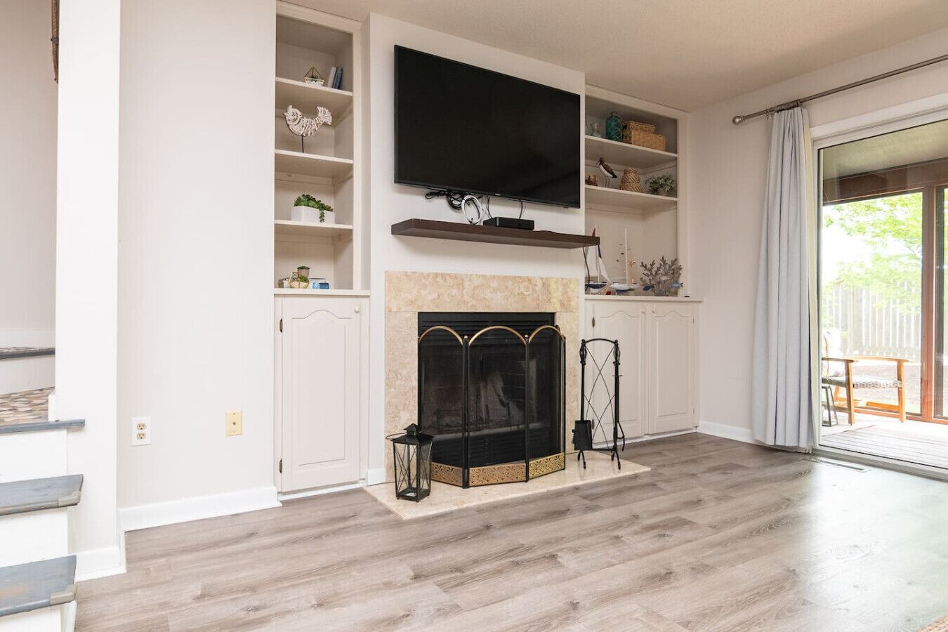 A living room with a fireplace, a flat-screen TV mounted above it, and a sliding glass door leading to an outdoor area.