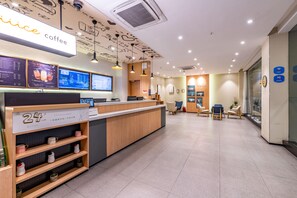 Interior de una cafetería con mostrador de recepción, pantallas digitales con el menú y zona de estar.