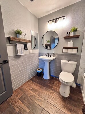 A bathroom with a white sink, a toilet, a mirror, and wooden shelves with plants.