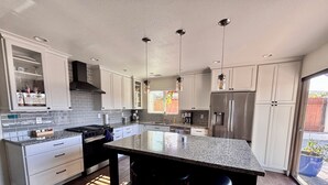 Cozinha moderna com armários brancos, bancada de granito, eletrodomésticos de aço inoxidável e uma ilha grande com banquetas.