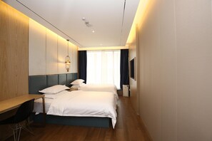 Habitación de hotel con dos camas, un escritorio, una silla, un televisor y una ventana con cortinas.