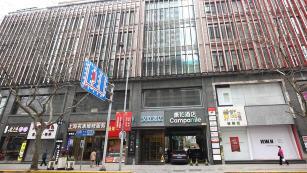 A modern building with large windows, a sign for a hotel, and various storefronts.