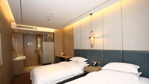 Habitación de hotel con dos camas, una mesita de noche con teléfono, una lámpara de pared y un baño con lavamanos y espejo.
