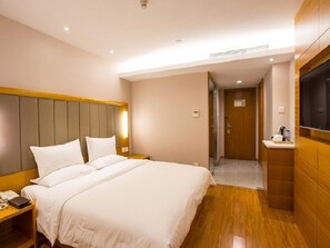 Hotellihuone, jossa on suuri sänky, yöpöydät, televisio ja puulattia.