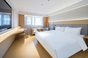 Et hotelværelse med en stor seng, et skrivebord, en stol, et lille bord og et fjernsyn.