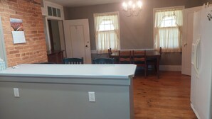 Une pièce avec un mur en briques, une porte blanche, un lustre, une table à manger avec des chaises et un réfrigérateur blanc.