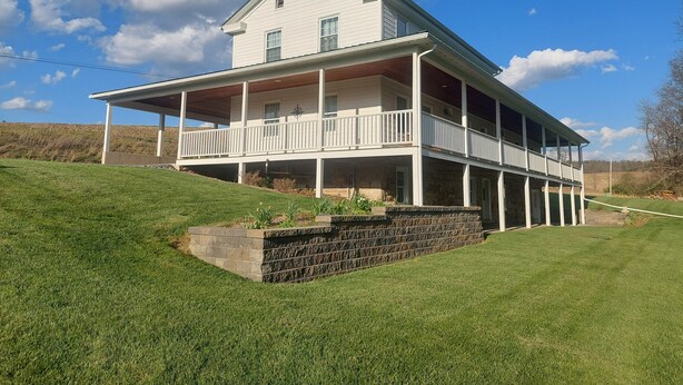 Une maison à deux étages avec un balcon, des fondations en pierre et une colline couverte d’herbe.