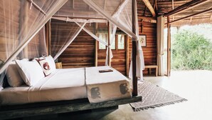 A bed with a canopy, wooden walls, and a view of greenery outside.