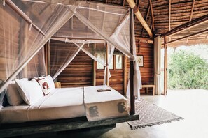Una cama con dosel, paredes de madera y vistas al exterior con vegetación.