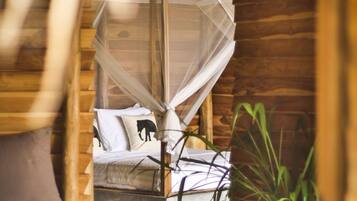 A wooden cabin interior with a bed, a mosquito net, and a plant.