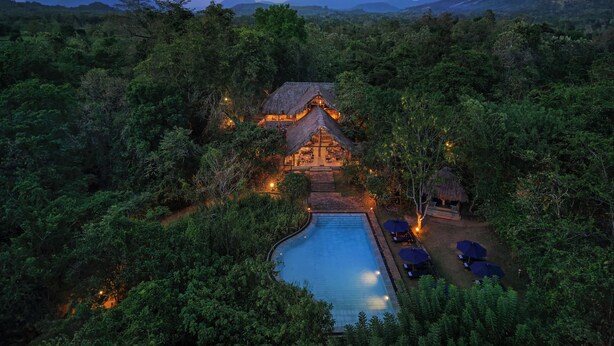 A thatched-roof building surrounded by dense forest, with a swimming pool and umbrellas. - Gal Oya Lodge (MADULLA)