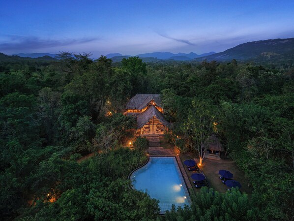 A thatched-roof building surrounded by dense forest, with a swimming pool and umbrellas. - Gal Oya Lodge (MADULLA)