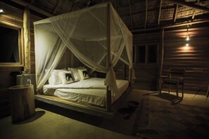 A four-poster canopy bed with pillows, a wooden bench, and a rustic interior. - Gal Oya Lodge (MADULLA)