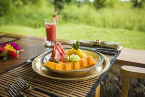Una mesa de comedor con un plato de fruta, un vaso de bebida y un arreglo floral.