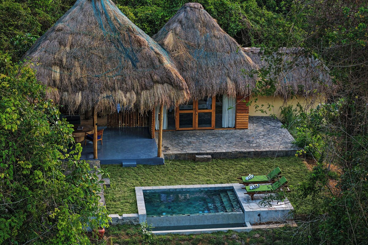 A thatched-roof bungalow with a pool and outdoor seating.