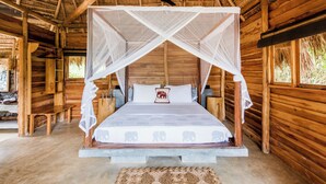 A wooden cabin with a bed under a mosquito net, a ceiling fan, and a woven mat on the floor. - Gal Oya Lodge (MADULLA)
