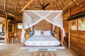 A wooden cabin with a bed under a mosquito net, a ceiling fan, and a woven mat on the floor. - Gal Oya Lodge (MADULLA)