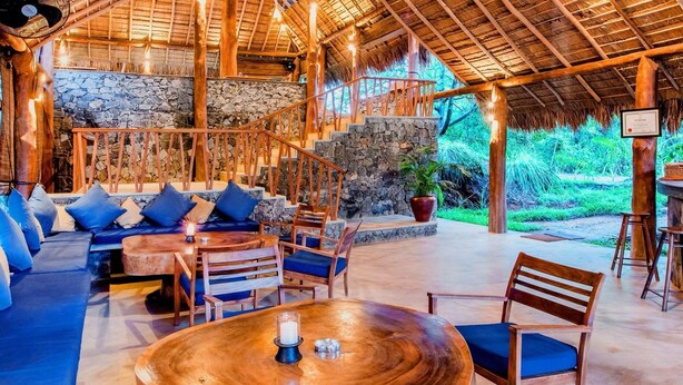 A wooden interior with a stone wall, a wooden staircase, and a seating area with cushions.