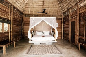Una habitación de madera con una cama bajo una dosel, un ventilador de techo y un banco.